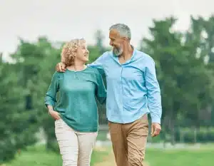 An elderly couple walking through a green forest, embracing each other.